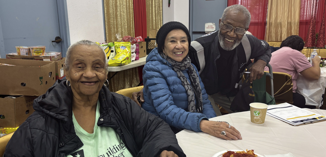 Three older adults sitting around a table, smiling.