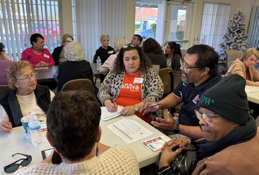 Group of older people sitting around a table, looking at paperwork and talking.
